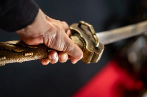 Detailaufnahme einer Hand, die den kunstvoll verzierten Griff eines Katana Schwerts hält – Symbol für japanische Handwerkskunst und traditionelle Schwertkunst.