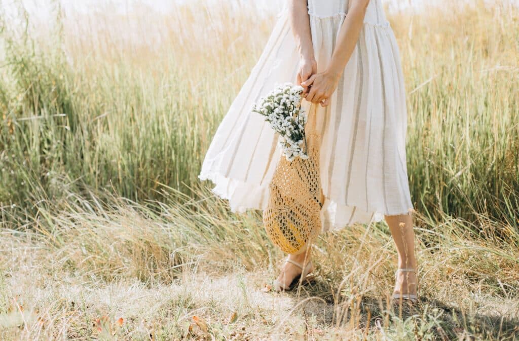 Eine Frau in einem weißen Sommerkleid und einer Tasche mit Blumen darin