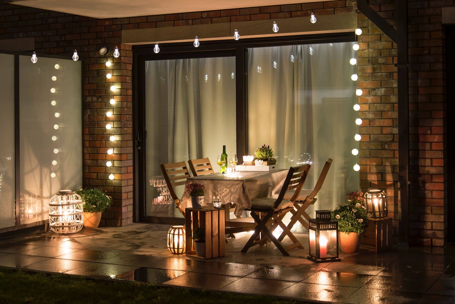 Eine stilvoll dekorierte Terrasse bei Nacht mit Holzstühlen, einem gedeckten Tisch und hängenden Lichterketten, ideal für Pavillons, um Schutz und Atmosphäre zu schaffen.