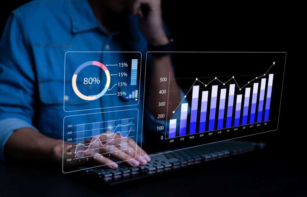 Eine Person arbeitet an einem Computer, während auf einem digitalen Dashboard Diagramme und Analysen einer ERP-Branchenlösung angezeigt werden.