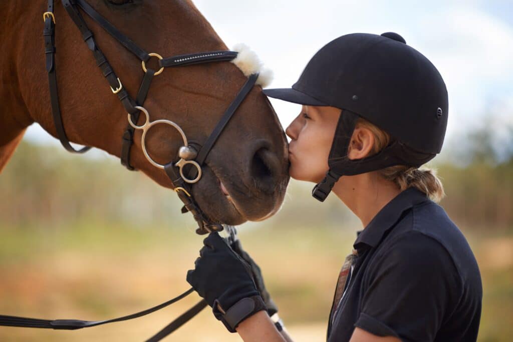 A rider wearing a helmet gently kisses her brown horse