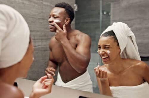 Zwei Personen tragen Gesichtspflege im Badezimmer auf und lachen dabei vor dem Spiegel