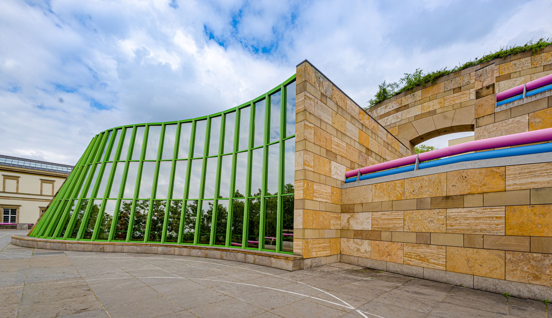 Fassade der Staatsgalerie Stuttgart mit gruener Glasstruktur und Sandsteinmauer im urbanen Kontext