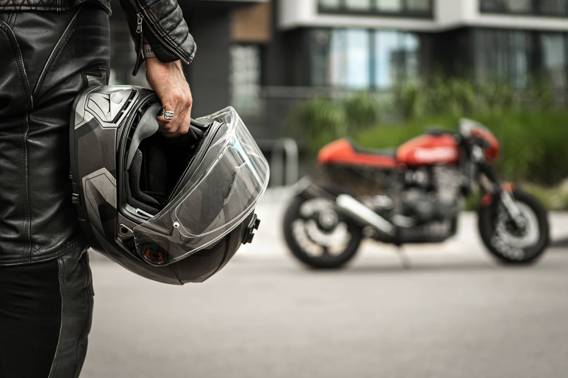 Biker hält Helm vor geparktem Motorrad in der Stadt | Topcase