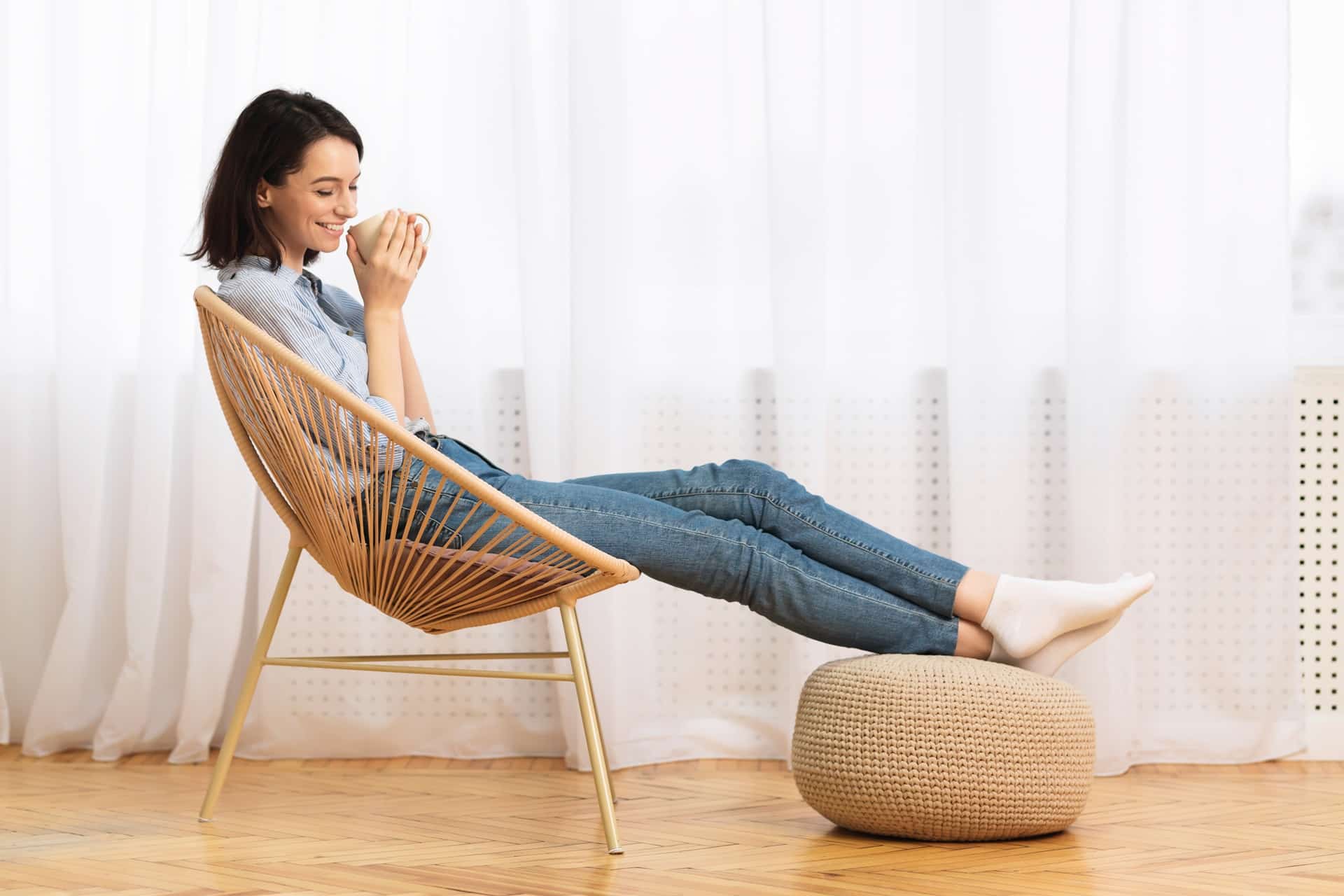 Junge Frau sitzt entspannt mit Tasse in heller Wohnung | Baufinanzierung Krefeld